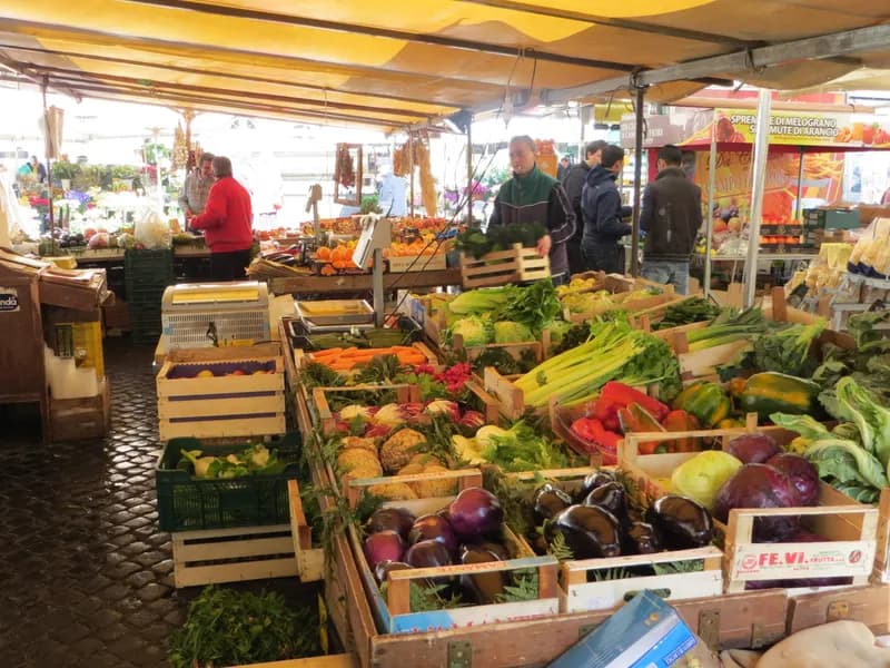 Banchi di frutta e verdura di un mercato coperto, con clienti e venditori