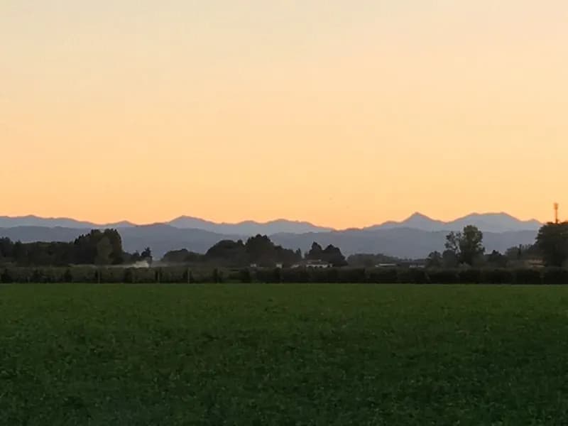 La pianura coltivata al tramonto, con il profilo delle montagne all’orizzonte