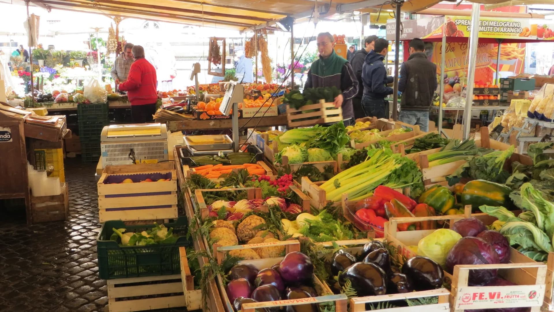 Banchi di frutta e verdura di un mercato coperto, con clienti e venditori